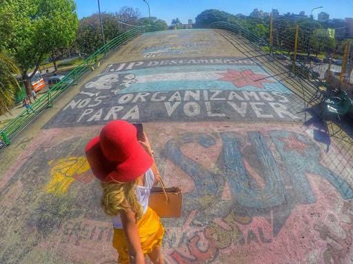Solo traveler in red hat taking smartphone photo of street art in Argentina